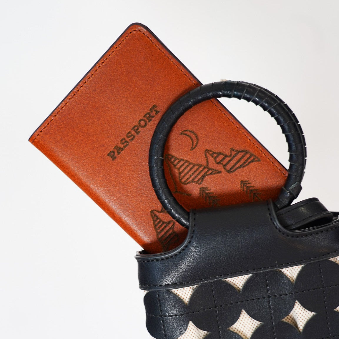 Black and white patterned handbag with a brown leather passport holder on a white background