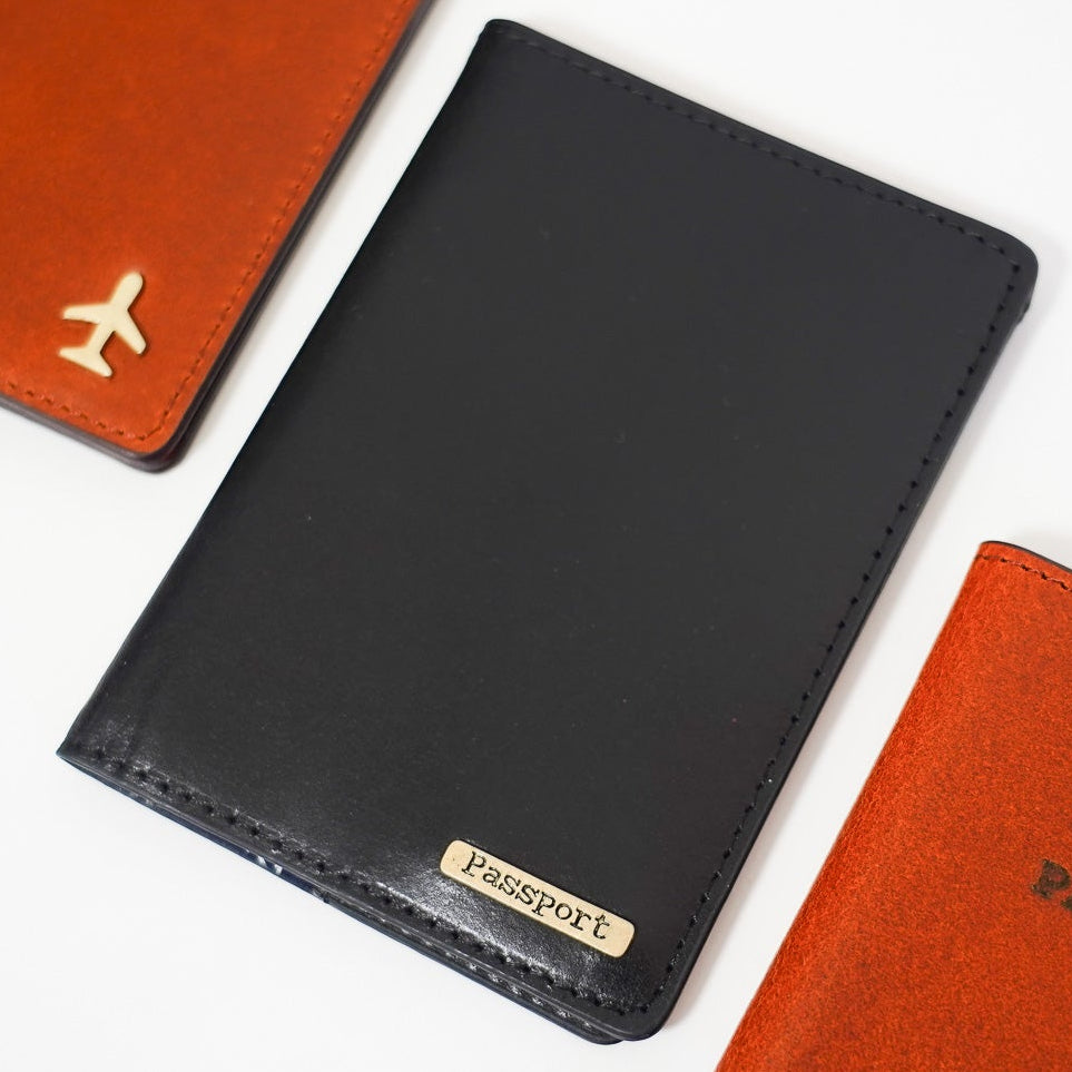 Three leather travel passport holder in black, orange, and red on a white background